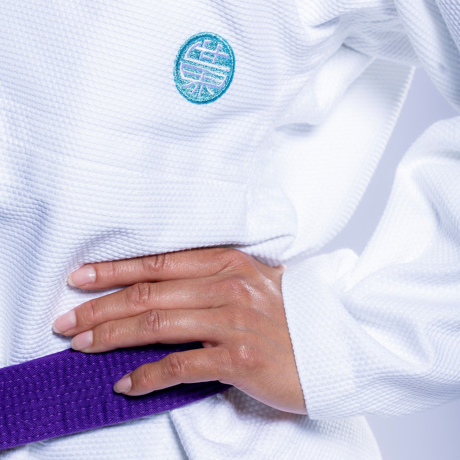 A person wearing the Womens SEKAI 3.0 BJJ Gi White Teal with a purple belt rests their hand on their hip.