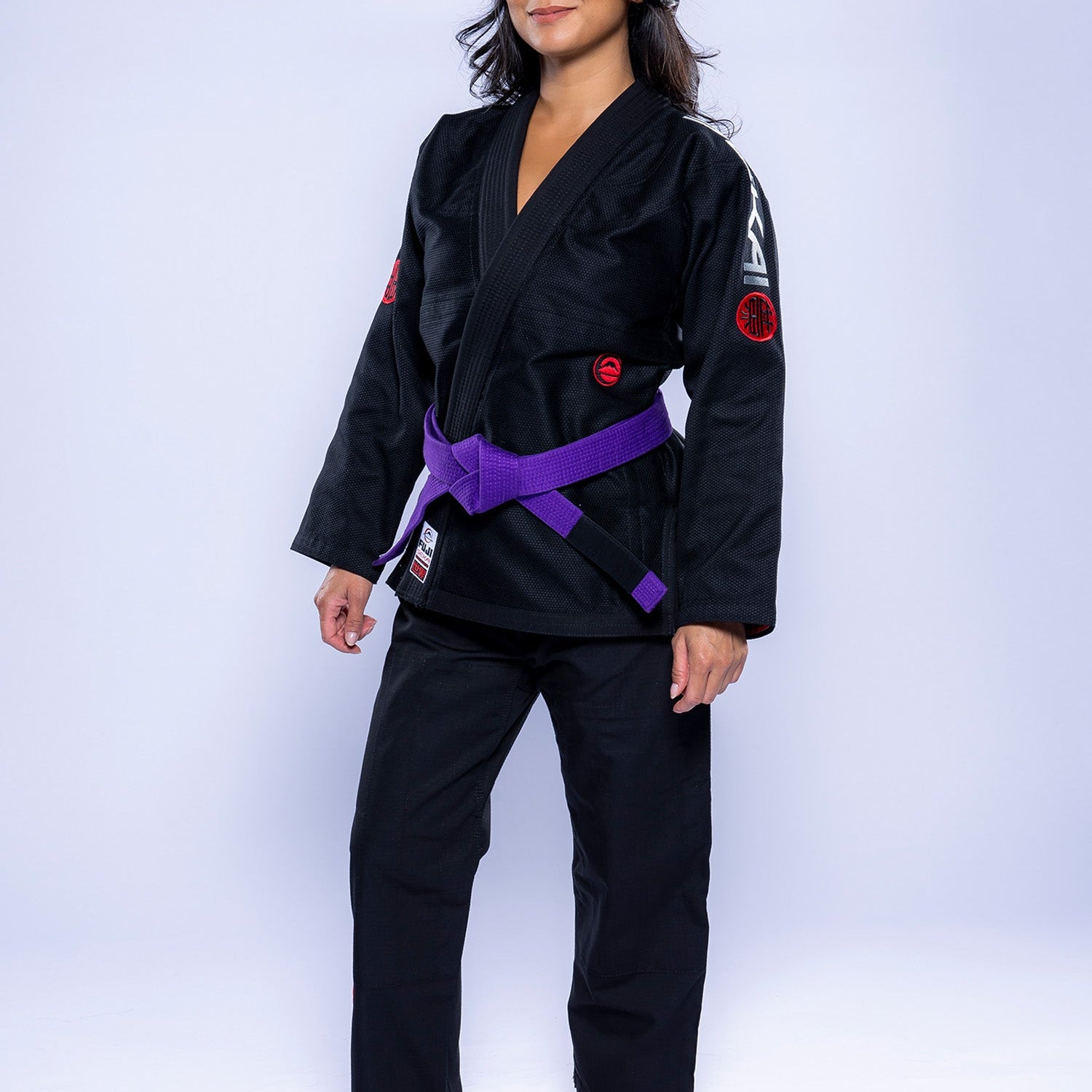 A woman stands barefoot on a white background, confidently wearing the Womens SEKAI 3.0 BJJ Gi Black Grey with a purple belt. She looks at the camera with a slight smile and a relaxed posture.