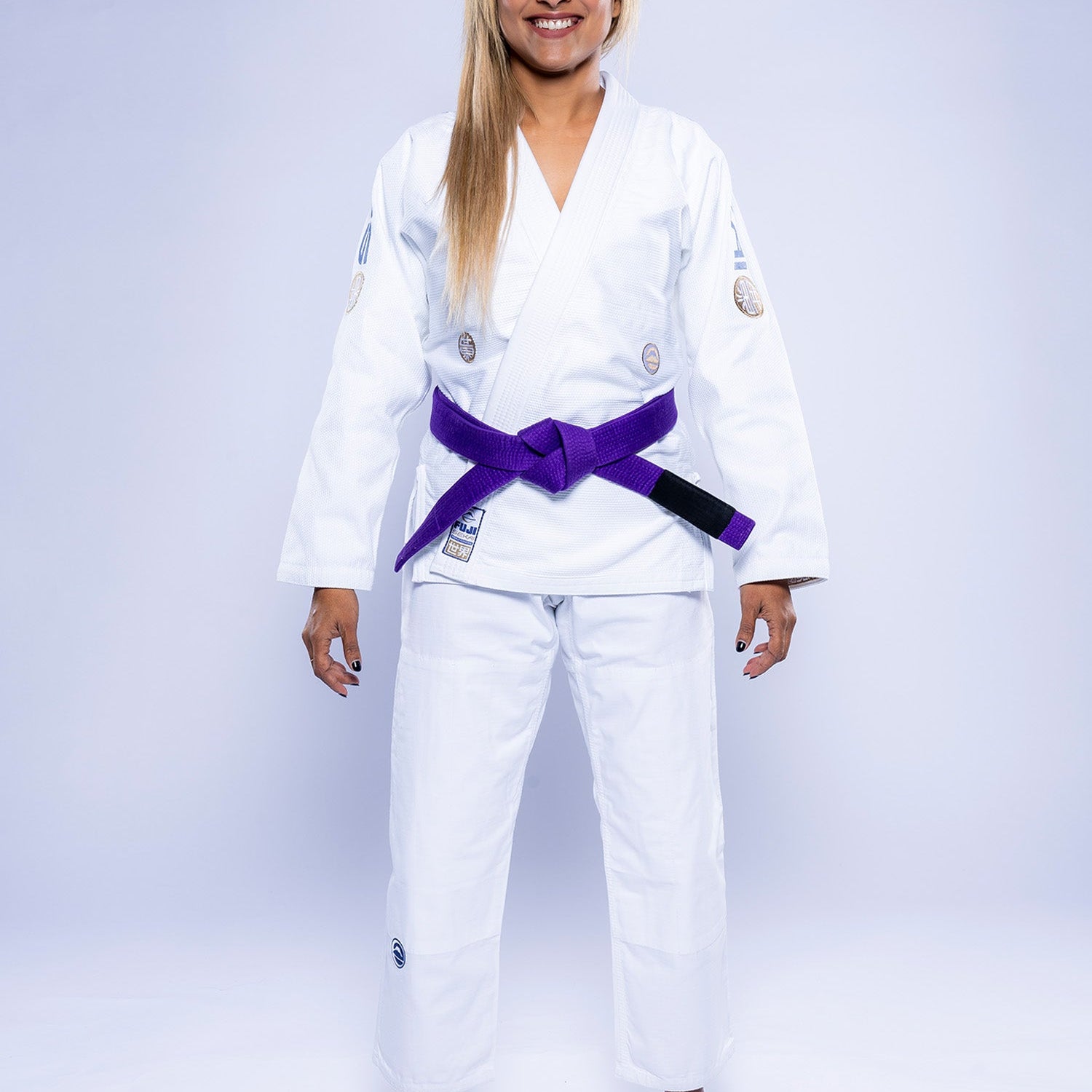 A woman stands barefoot, smiling, wearing the Womens SEKAI 3.0 BJJ Gi White Navy with a purple belt against a plain light background.