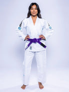 A woman stands barefoot, hands on hips, facing forward in a Womens SEKAI 3.0 BJJ Gi White Teal with a purple belt against a plain light background.