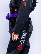 A person wears the Womens SEKAI 3.0 BJJ Gi Black Grey, standing against a plain background with their left arm, torso, and leg partially visible.