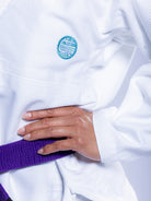 A person wearing the Womens SEKAI 3.0 BJJ Gi White Teal with a purple belt rests their hand on their hip.