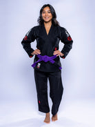 A woman with long dark hair stands barefoot, smiling with hands on hips, wearing the Womens SEKAI 3.0 BJJ Gi in black grey with a purple belt, against a light background.