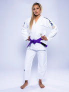 A woman stands confidently barefoot, hands on hips, wearing the Womens SEKAI 3.0 BJJ Gi White Navy with a purple belt against a plain light background.