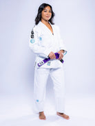 A woman stands barefoot against a white background, confidently holding a purple belt while wearing the Womens SEKAI 3.0 BJJ Gi White Teal with patches.
