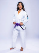 A woman stands barefoot in the Womens SEKAI 3.0 BJJ Gi White Teal with a purple belt, confidently looking to the side against a plain light background.